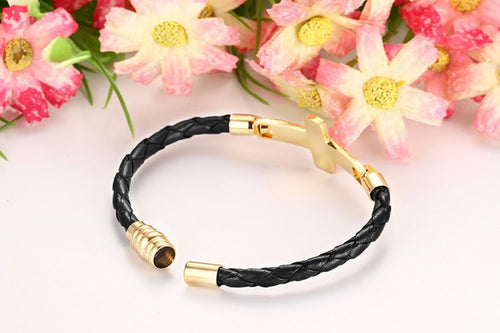 Black braided bracelet with gold accents on a white background with pink flowers.