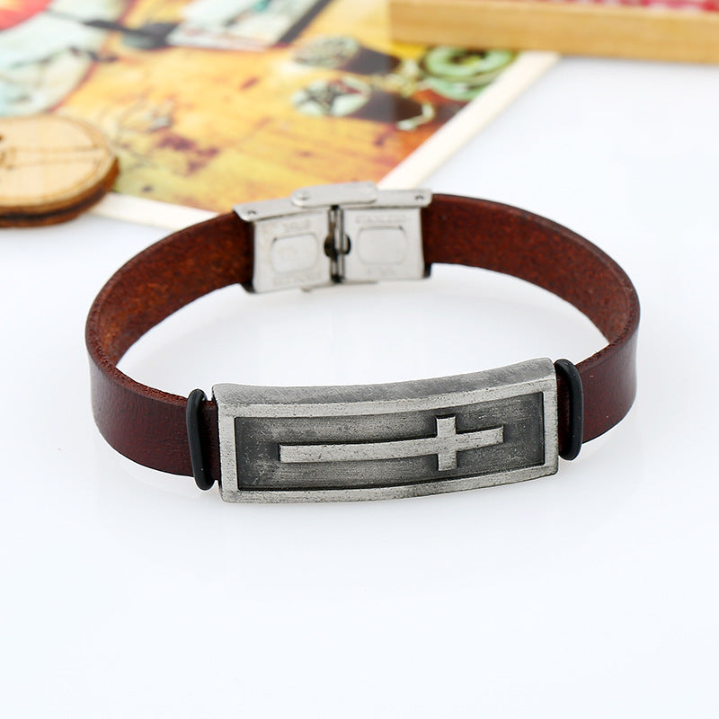 Brown leather bracelet with metal clasp and cross emblem on a white surface