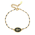 Gold bracelet with black beads and a central black disc featuring a gold cross on a white background.
