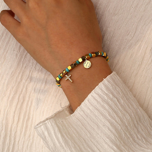 Hand wearing a beaded bracelet with various charms on a light background